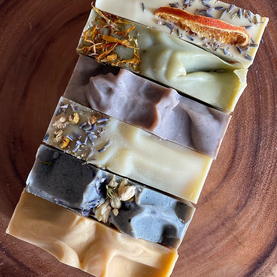 Six handmade soap bars lined in a row at a 45 degree angle to the right.  The soaps are naturally colored with clays and botanicals, and handmade using the cold process method, in small batches.  Tiffany Riffer Soap is based in Washington, DC.