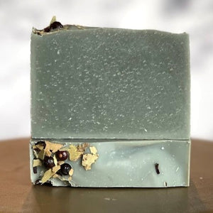 Two bars of eucalyptus bar soap, one laying flat with the top facing the viewer.  The other bar sits on top of the first, with the widest surface area facing the viewer to show the soft light gray color of the soap.  This soap is scented with all natural eucalyptus essential oil and colored with a touch of activated charcoal. 
