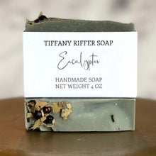 Load image into Gallery viewer, Two bars of eucalyptus bar soap, one laying flat with the top facing the viewer. The other bar sits on top of the first, with the widest surface area facing the viewer to show the front side of the soap label with branding by Tiffany Riffer Soap.. This soap is scented with all natural eucalyptus essential oil and colored with a touch of activated charcoal.

